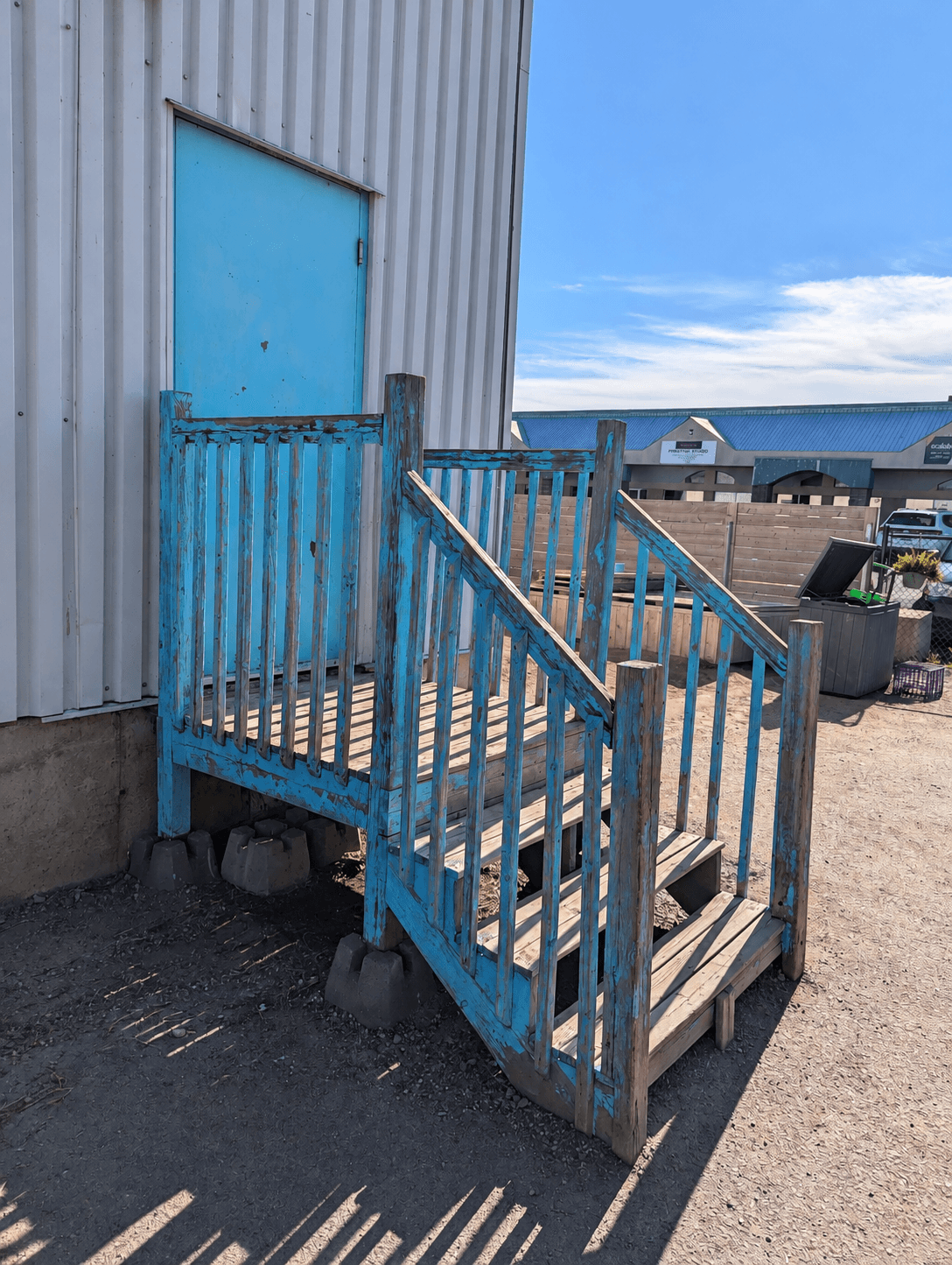 Weathered exterior wood stairs and railing with peeling blue paint, beside a metal-sided building