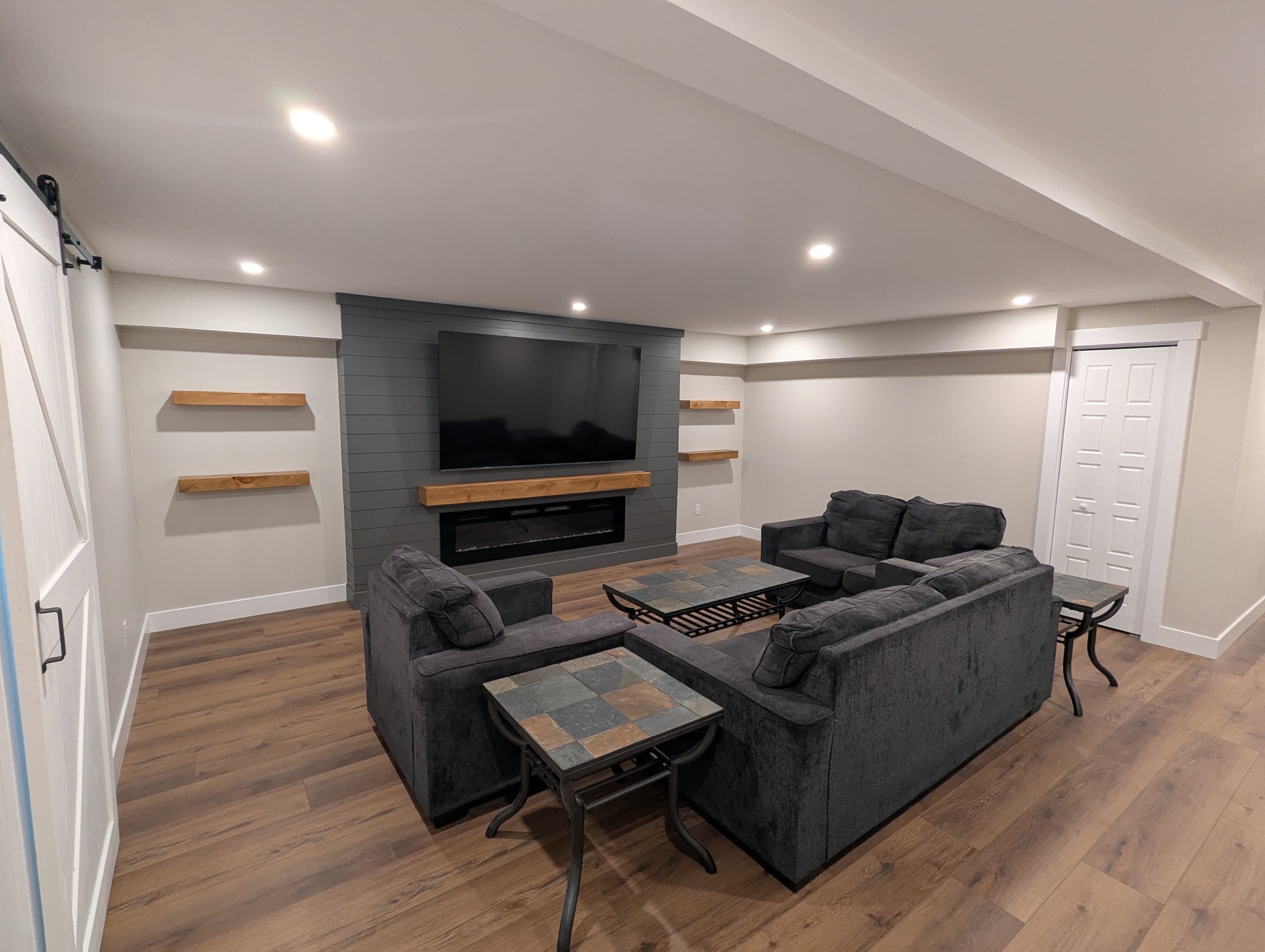 Finished basement family room with sectional seating, a media wall with fireplace and mounted TV, and floating shelves